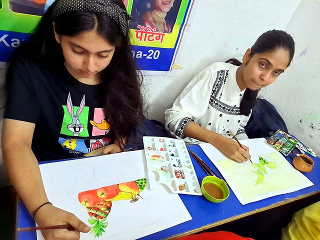 Two students painting and drawing on sheets at a table